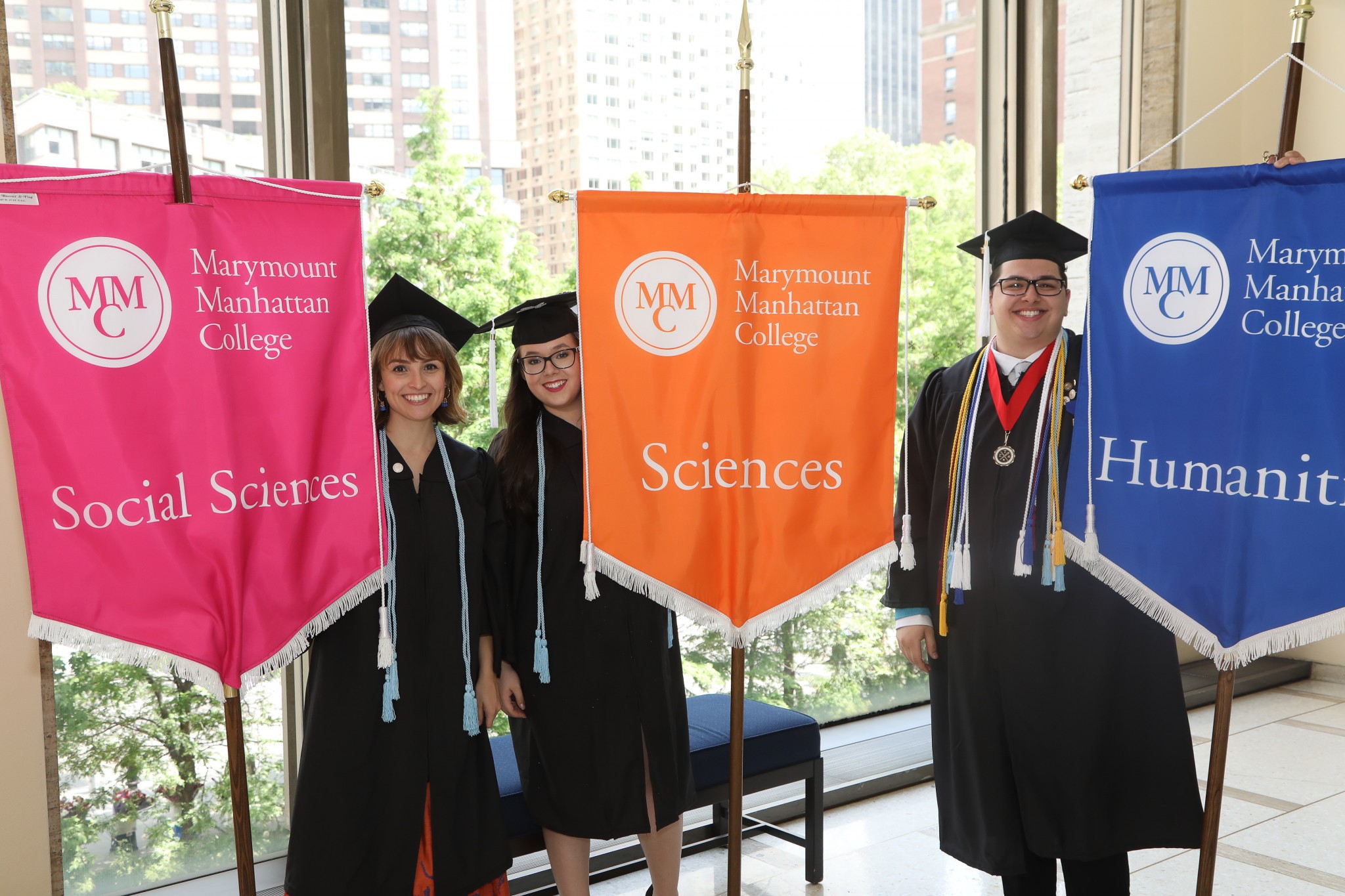 Three students at Commencement holding banners with the names of Majors on them