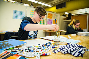 Close-up of student painting a piece in the Art Studio; another student working farther away from him