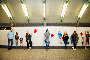 MMC students standing in the subway station in front of a wall design with balloons and children on it