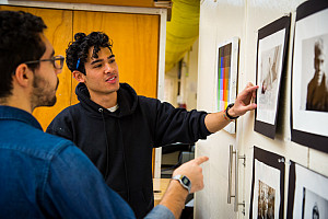 Student and his professor looking at a display of paintings hung up on a wall in the Art Studio