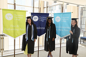 Three graduating students holding MMC banners with the names of subject fields on them at Commencement 2017